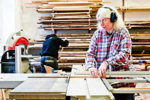 Frau arbeitet mit Hörschutz an Holzkreissäge am Standort Wurlitzergasse © Kollektiv Fischka/fischka.com Frau arbeitet mit Hörschutz an Holzkreissäge am Standort Wurlitzergasse © Kollektiv Fischka/fischka.com